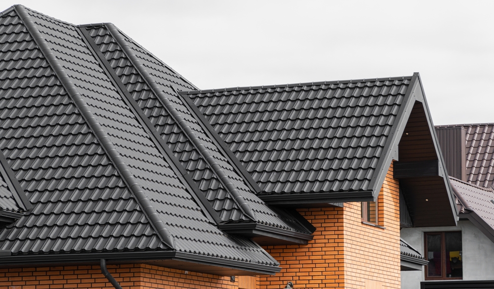 The image shows the roofs of several houses with black metal roofing tiles. The walls are made of yellow and orange bricks. The architectural style features multiple gables and steep slopes.