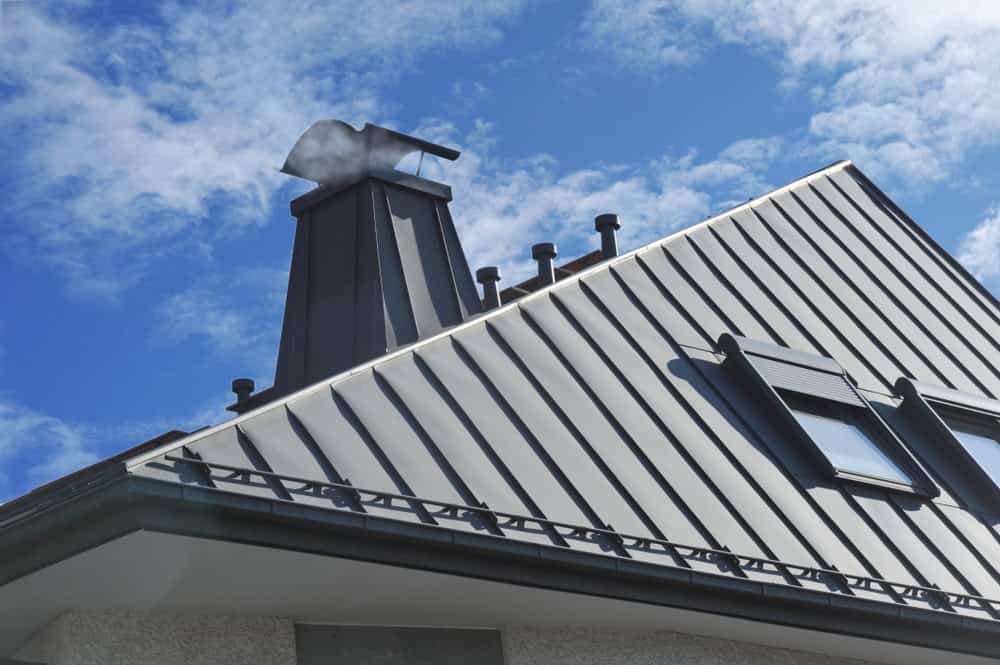 A modern building with a sloped metal roof featuring a rooftop chimney cap shaped like a bear. The sky is bright and partly cloudy.
